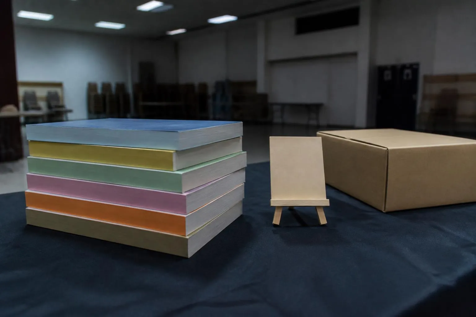 Pile de tomes de manga posée sur une table de stand, tranches colorées tournées vers l'objectif, sous un néon de salle polyvalente